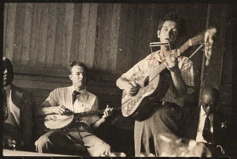 Pete Seeger (banjo) sentado e Woody Guthrie (gaita e violão) em pé